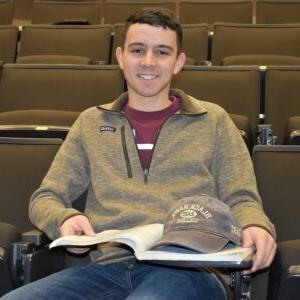 student sitting in theater room with book open on lap and hat resting on book